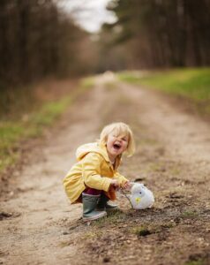 黄色いレインコートを着た男の子が、道にしゃがみこんで何かを見つけて喜んでいる様子。